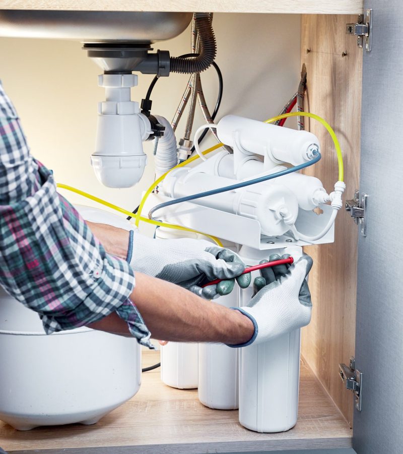 Plumber hand in gloves replace water filter cartridges at kitchen. Fix purification osmosis system. Technician installing or repairing system of water filtration.